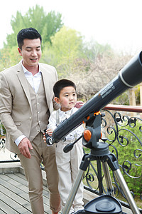 父亲和儿子在阳台使用天文望远镜图片