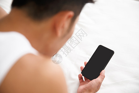 25岁到29岁男20多岁青年男人在卧室玩手机图片