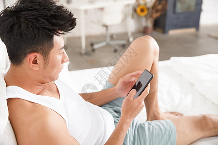 舒适开端背心青年男人在卧室玩手机图片