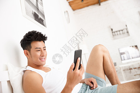 水平构图舒适时尚青年男人在卧室玩手机图片