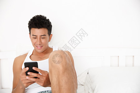 白昼幸福独处青年男人在卧室玩手机图片