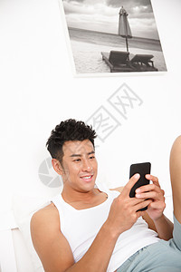 坐着活力无忧无虑青年男人在卧室玩手机图片