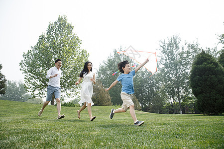 东方人放风筝独生子家庭一家三口在草地上奔跑图片