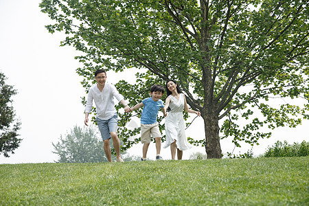 青年女人休闲学龄前儿童一家三口在草地上奔跑图片