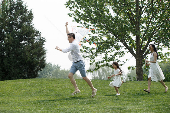 青年男人双亲家庭公园一家三口在草地上放风筝图片
