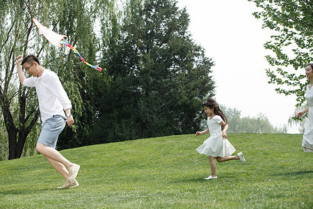 休闲家庭独生子家庭一家三口在草地上放风筝图片