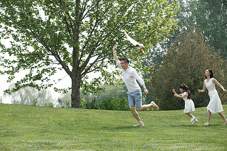 愉悦家庭生活郊游一家三口在草地上放风筝图片