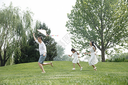 愉悦家庭奔跑一家三口在草地上放风筝图片