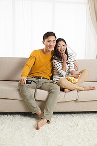 20多岁东亚青年情侣坐着沙发上看电视图片