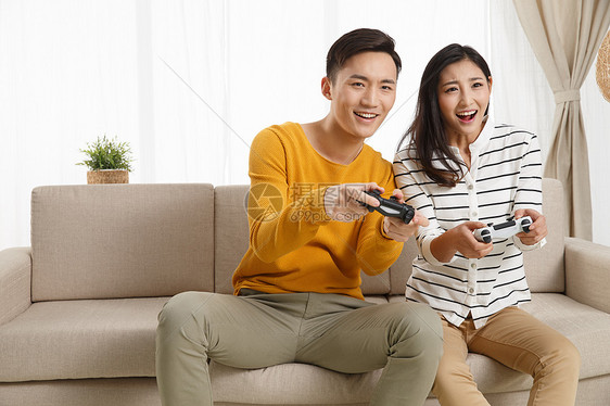 青年夫妇25岁到29岁满意青年情侣坐着沙发上玩游戏图片