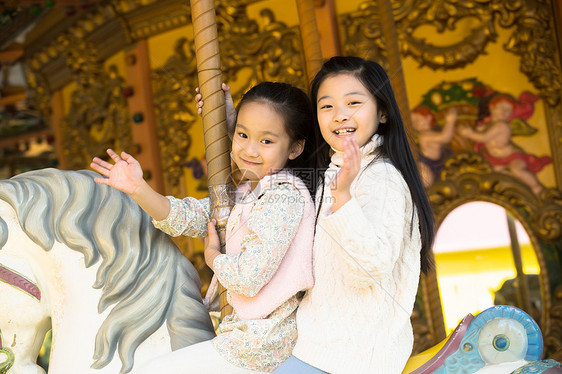 坐着游乐园设施学龄儿童两个小女孩在玩旋转木马图片