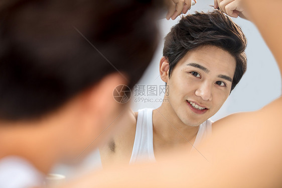 笑欢乐反射照着镜子给头发喷啫喱的年轻男人图片
