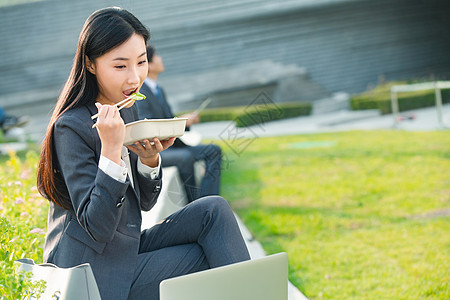 商务女性坐着户外边吃饭边工作图片