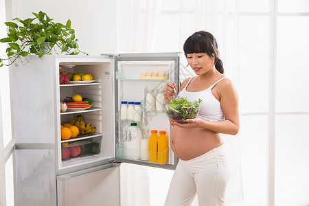 健康的快乐渴望孕妇打开冰箱拿蔬菜图片