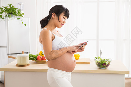 休闲装开放式厨房青年女人孕妇看平板电脑图片