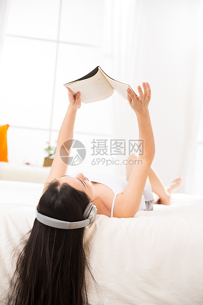 放松摄影知识青年女人躺在床上听音乐看书图片