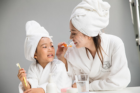 牙刷毛巾希望可爱的成年人穿着浴袍的母女刷牙背景