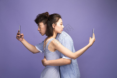 紫色背景表情相伴各自玩手机的青年情侣图片