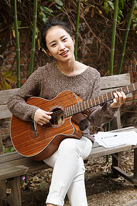 坐着摄影庭院快乐的年轻女人弹吉他图片