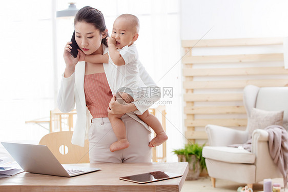 年轻妈妈抱着孩子在家办公图片