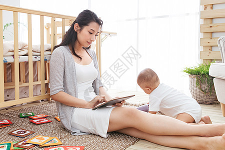 快乐年轻妈妈在家边看孩子边使用电脑图片