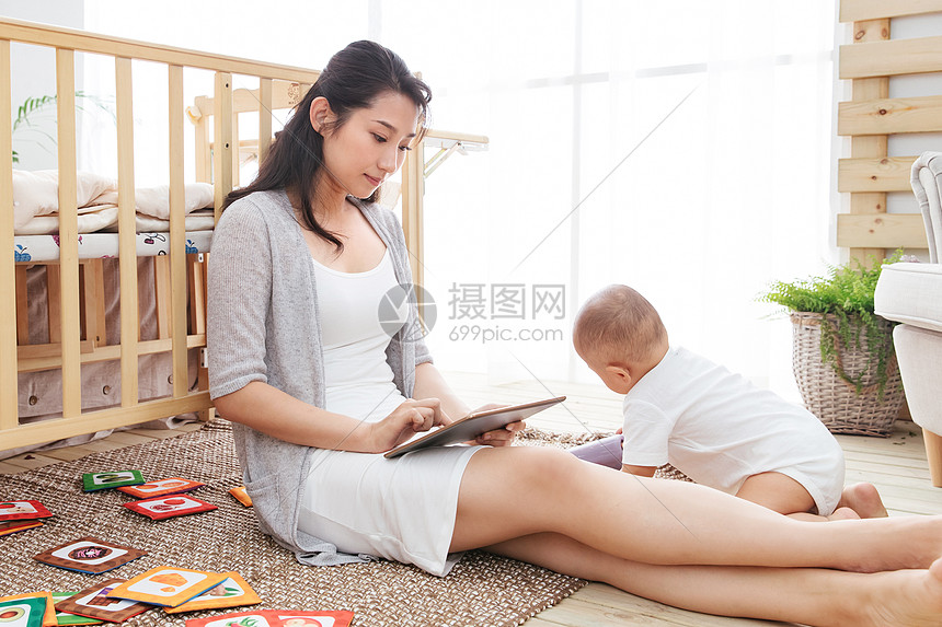 快乐年轻妈妈在家边看孩子边使用电脑图片