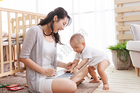 年轻妈妈在家边看孩子边使用电脑图片