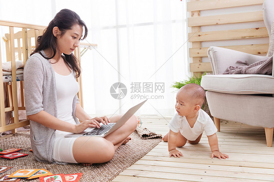 年轻妈妈在家边看孩子边使用电脑图片