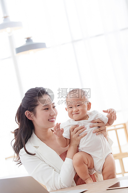 年轻妈妈抱着孩子在家办公图片