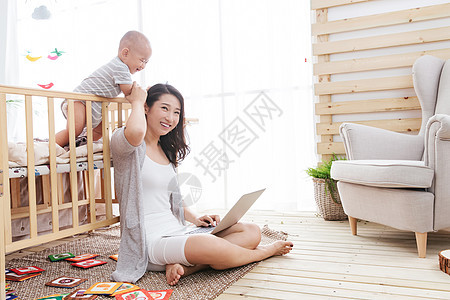 年轻妈妈在家边看孩子边使用电脑图片