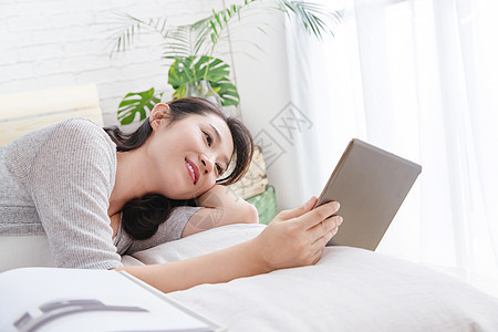 水平构图愉悦清新青年女人躺在床上看平板电脑图片