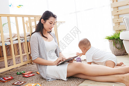 婴儿户内不看镜头年轻妈妈在家边看孩子边使用电脑图片