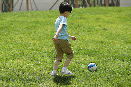 户外跑步小男孩在草地上踢球背景