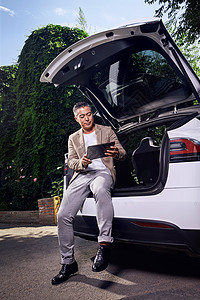 商务旅行成熟男士坐在汽车后备箱里看平板电脑图片