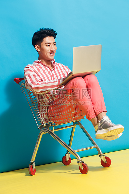 智慧享乐东亚青年男人坐在购物车里用笔记本电脑图片