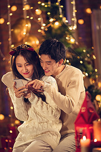 节日温暖鹿角幸福的年轻伴侣在家玩手机图片