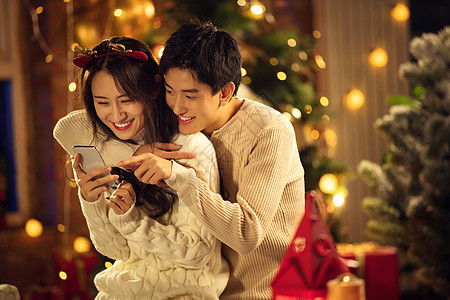 圣诞节东方人男朋友幸福的年轻伴侣在家玩手机图片