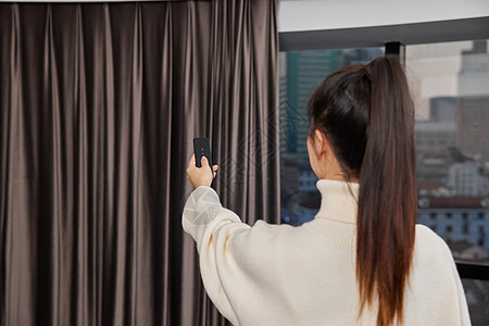 年轻女性使用遥控操作智能窗帘背影图片