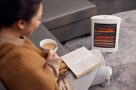居家女性在取暖器旁看书喝咖啡高清图片