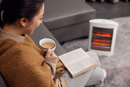 冬日女性在取暖器旁看书喝咖啡图片