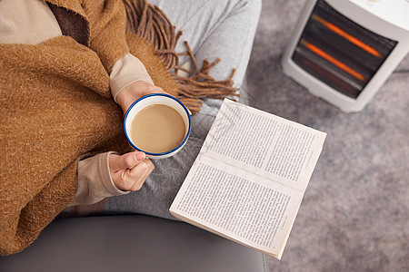 冬日女性在取暖器旁看书喝咖啡特写图片