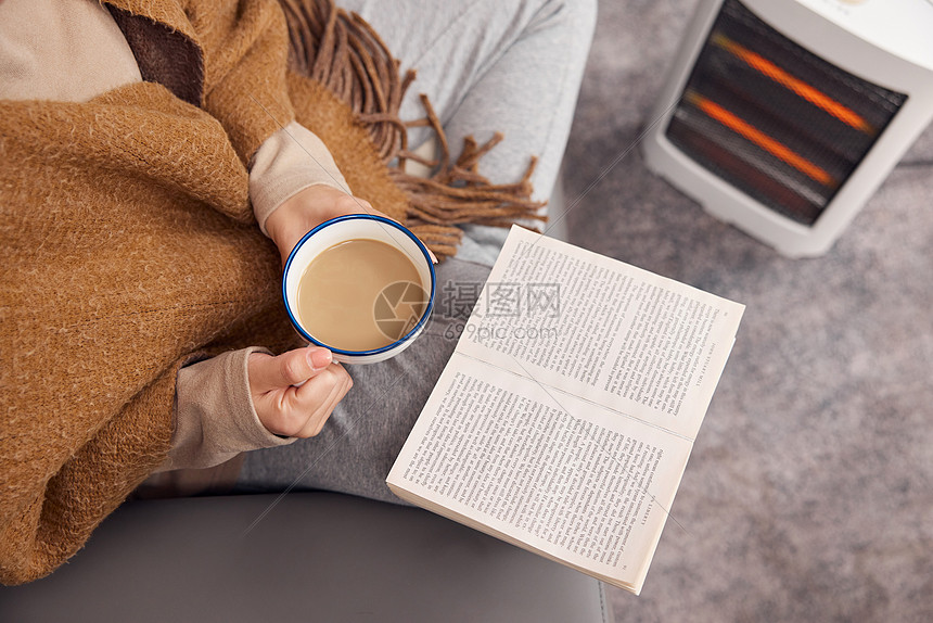 冬日女性在取暖器旁看书喝咖啡特写图片