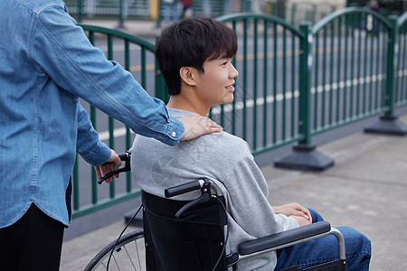 亲人陪伴坐轮椅的青年男性外出背景图片