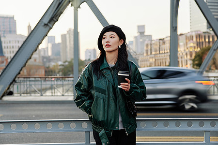 手捧咖啡站在桥上看风景的青年女性图片