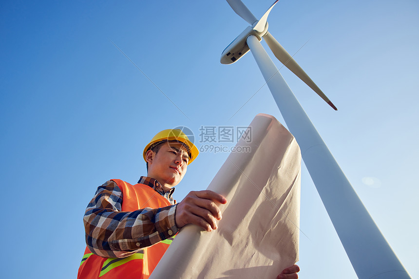 仰拍男性工程师在大风车下看图纸图片