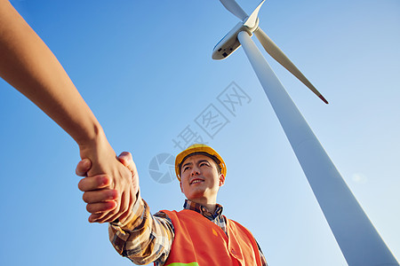仰拍工程师在大风车下握手合作图片