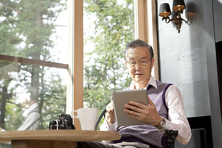 老年男性独自居家喝茶看平板电脑图片