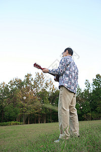 户外草地上中老年男性弹吉他背景图片