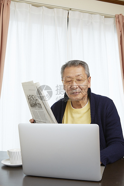 老年男性居家看报纸和电脑图片