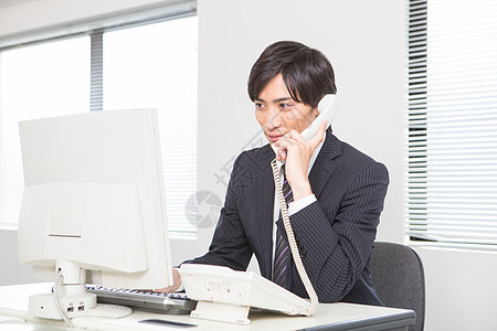 在电脑工位上给客户打电话的职场男性图片